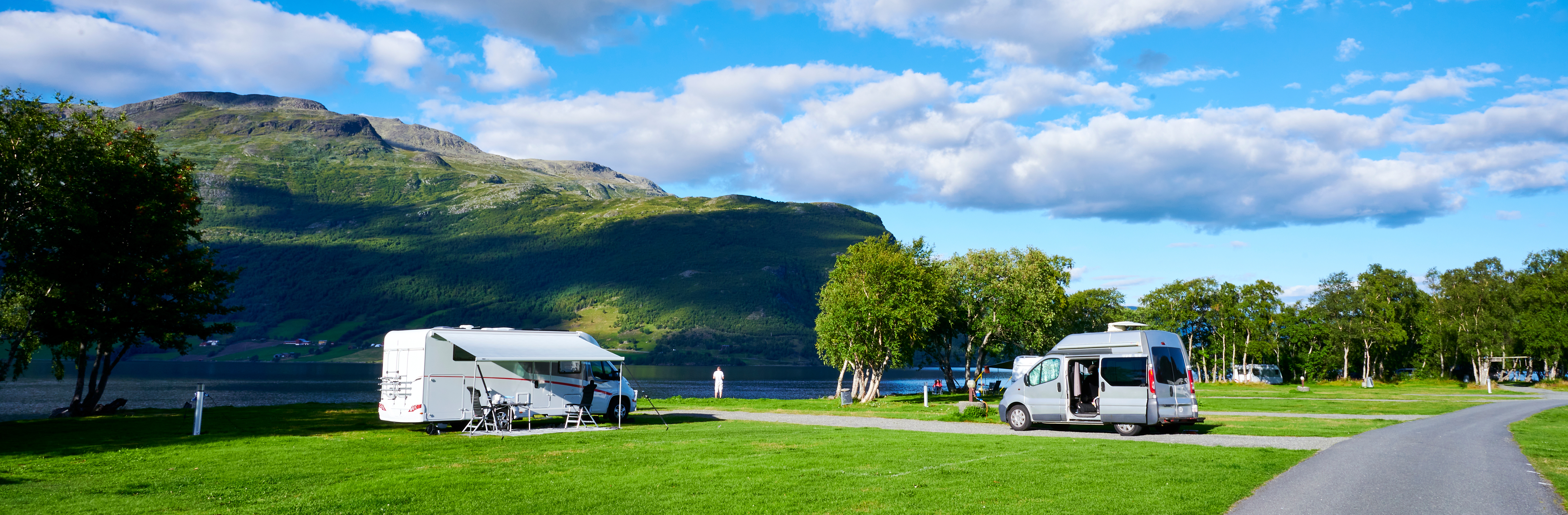 two motor homes on green grass with hill in the background